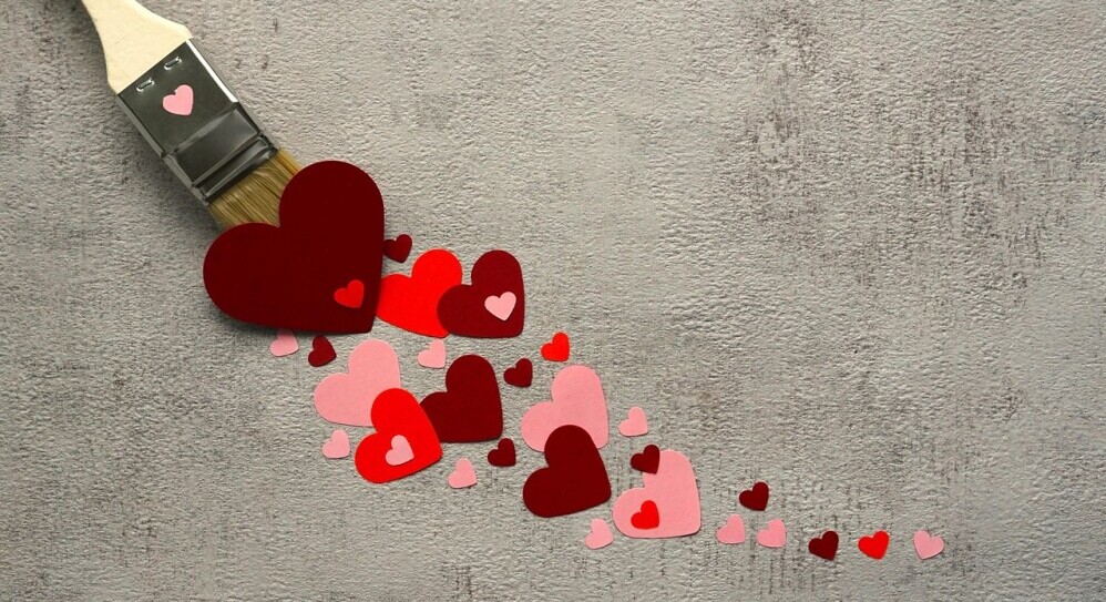 Paintbrush releasing red and pink heart shapes across a textured gray background, symbolizing creativity, care, and love.